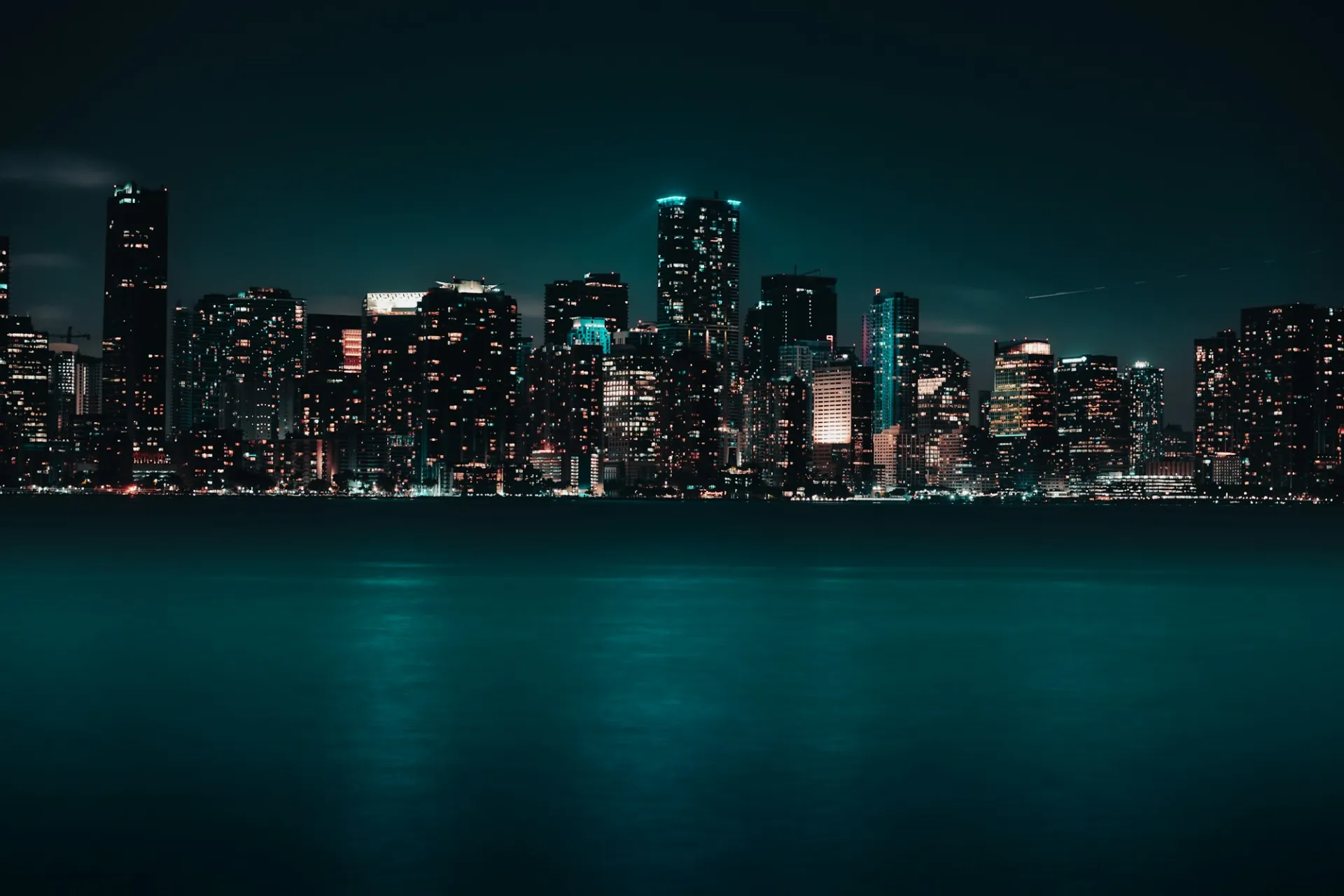 The lit Miami skyline at night, the water of the bay in front of it