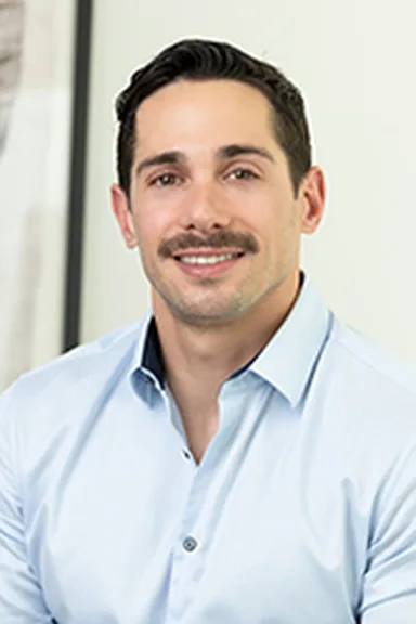Ryan Pruitt in a light blue shirt against a light background, smiling