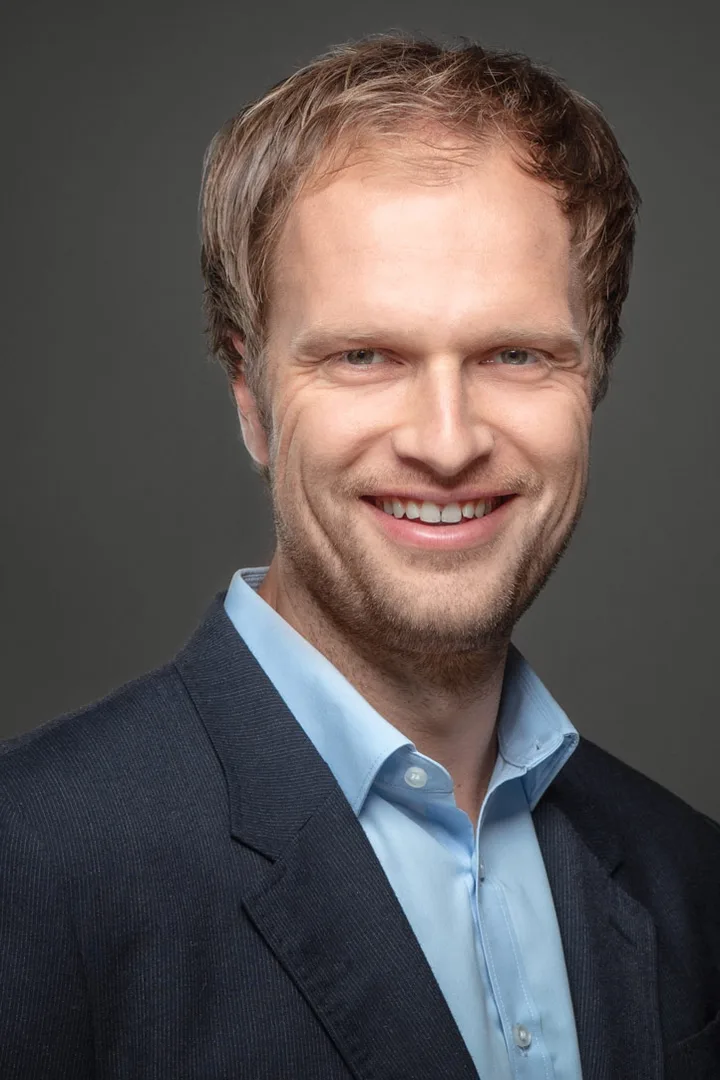 Thomas Render in a suit against a grey backdrop, smiling